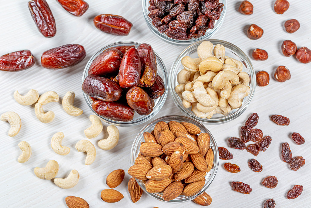 Dried fruits and nuts in small glass bowls on a white wooden table.