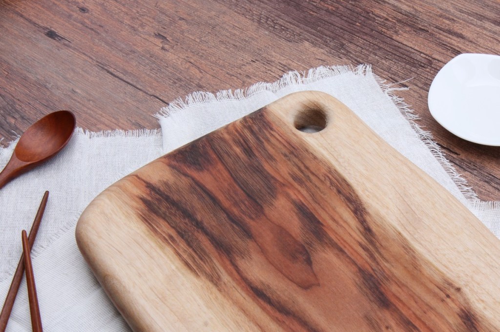 Wooden cutting board and utensils laying on a table.
