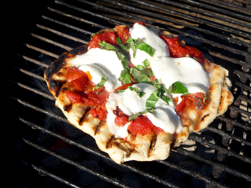 Pizza with mozzarella and basil on a grill.